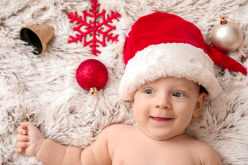 Obraz na płótnie Canvas Cute little baby in Santa Claus hat lying on plaid