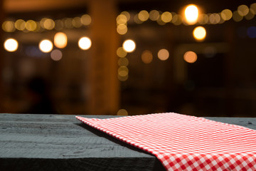 Empty wooden deck table with tablecloth over bokeh background