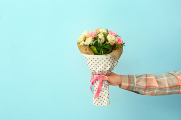 Hand of female florist with beautiful bouquet on color background
