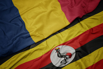 waving colorful flag of uganda and national flag of chad.