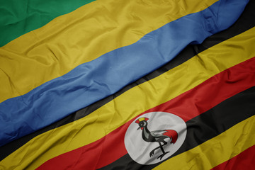 waving colorful flag of uganda and national flag of gabon.