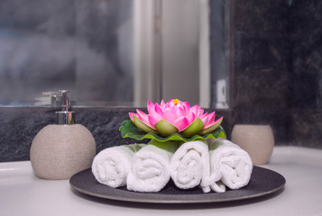 Rolled up white  towels with lotus flower decoration in grey bathroom. Spa interior.