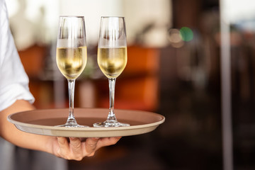 Hand of the waiter brings glasses with champagne on a tray.