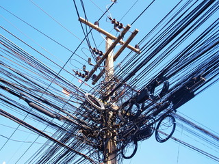 Messy cables, electric cables tangled on electrical poles On the blue sky background