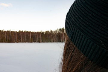 The girl looks at the winter forest on the lake.