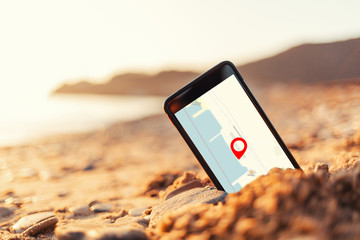 Concept of Internet maps and navigation. A smartphone buried in the sand on the beach shows...