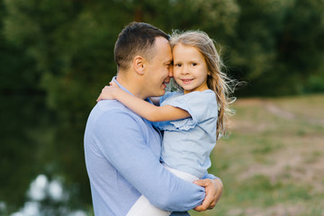 Fototapeta premium Dad holds his daughter in his arms, they are happy and smiling. Friendly relations between parents and children