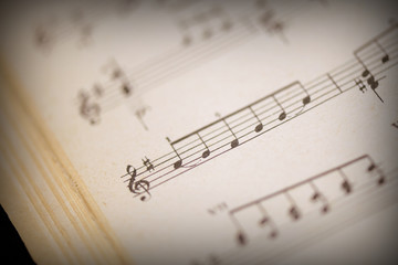 Fototapeta premium Fragment of a page from an old musical notebook on a dark surface close-up. Music background retro style toned