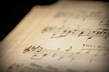 Fragment of a page from an old musical notebook on a dark surface close-up. Music background retro...