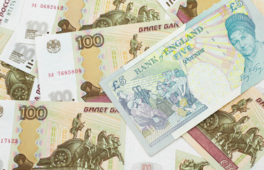 A close up image of a multicolored five pound note from the United Kingdom on a background of Russian one hundred ruble bills in macro
