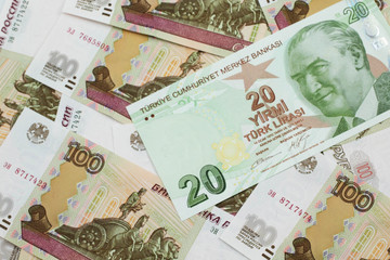 A close up image of a green twenty Turkish lira bank note on a background of Russian one hundred ruble bank notes in macro