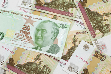 A close up image of a green twenty Turkish lira bank note on a background of Russian one hundred ruble bank notes in macro