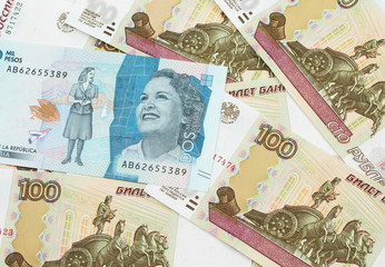 A close up image of a blue two thousand Colombian peso bank note on a background of Russian one hundred ruble bank notes in macro