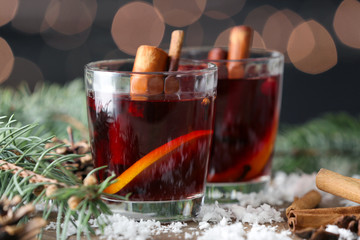 Glasses of tasty mulled wine, fir branches and snow on table