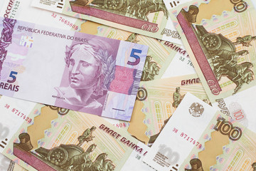A pink five reais bank note from Brazil close up in macro with a background of United States one dollar bills