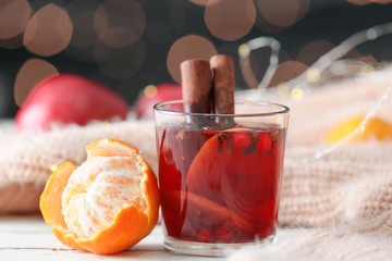 Glass of tasty mulled wine, tangerine and warm plaid on table