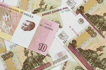 An red and white ten Angolan kwanza bank note on a background of Russian one hundred ruble bank notes