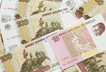 An red and white ten Angolan kwanza bank note on a background of Russian one hundred ruble bank notes