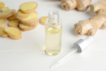 Bottle with ginger essential oil on white table