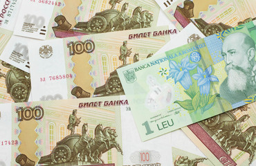 A close up image of a green Romanian one leu bank note on a background of Russian one hundred ruble bank notes