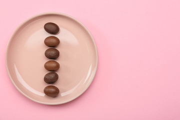 Plate with chocolate Easter eggs on color background