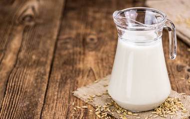 Old wooden table with fresh Oat Milk (close-up shot; selective focus)