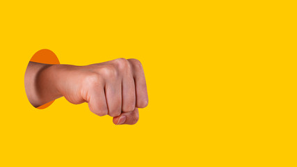 Young womans hand clenched into a fist. Hand sticks out of hole with sharp edges on vibrant yellow background. Equal rights for women concept. Copy space. Banner format.