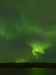 Northern lights over the lake and hills. Aurora at night in the sky in the north.