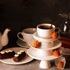 White dish pyramid with cup of tea on top decorated with chocolate truffles on surved dessert table on dark background. Creative concept, restaurant, candy shop. Horizontal for wallpaper, postcard