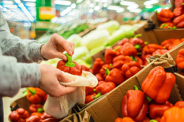 Shopping at the supermarket. The girl in the store chooses peppers in the vegetable department. A healthy and balanced diet.