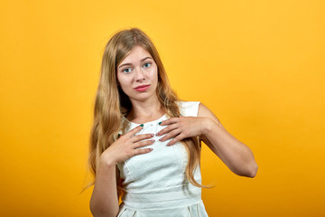 Attractive blonde young caucasian woman holding hands on chest, looking at camera over isolated orange background wearing white shirt. Lifestyle concept