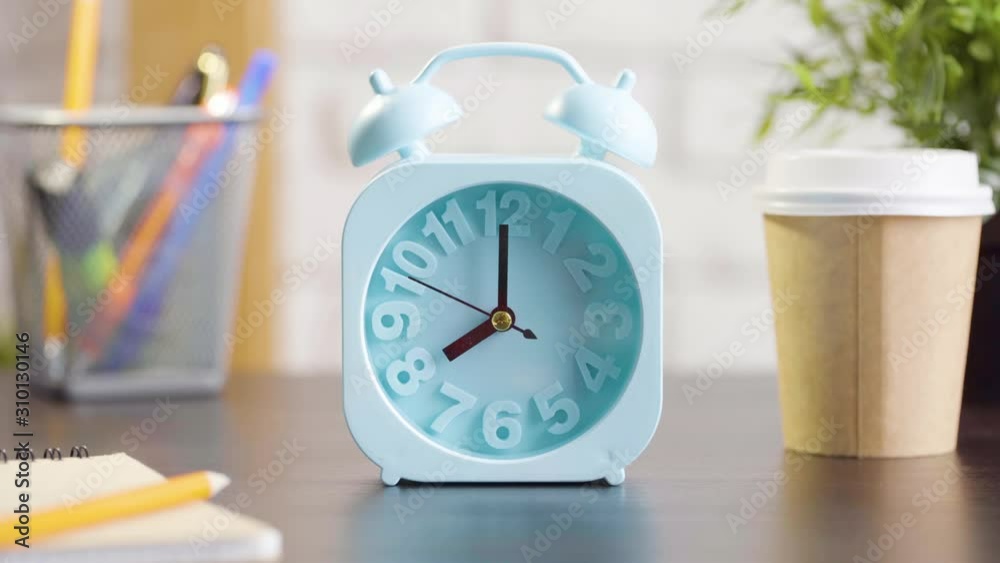 Wall mural Blue alarm clock showing 8 o'clock. Hand taking a cup from table