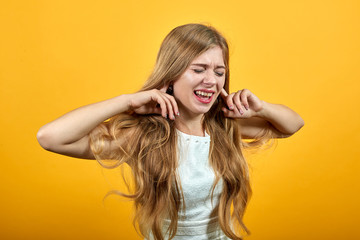 Fototapeta premium Dissatisfaction caucasian blonde young woman keeping fingers on ears, looking confused with closed eyes over isolated orange background wearing white shirt. Lifestyle concept