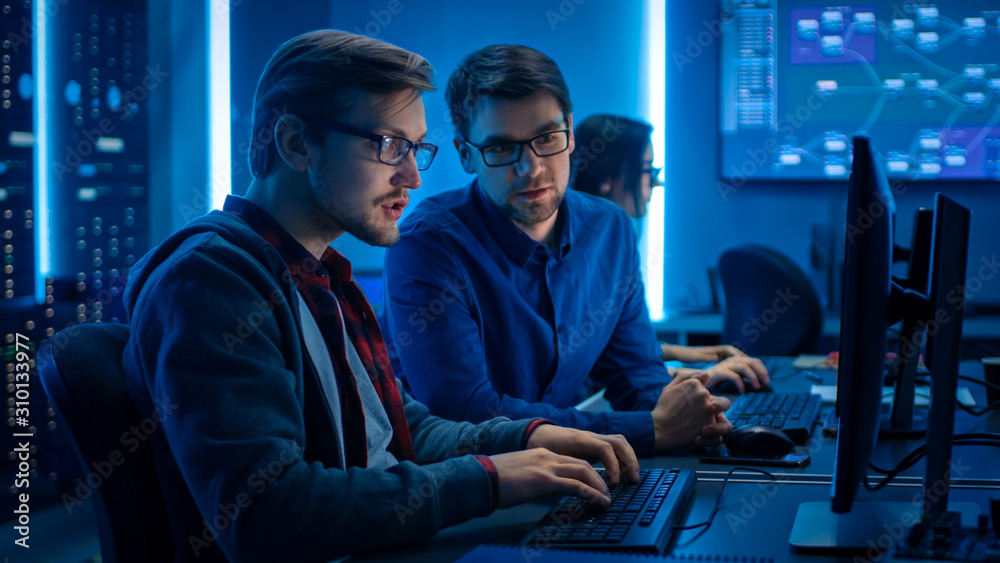 Poster Two Professional IT Programers Discussing Technical Data Show on Desktop Computer Display. Working Data Center Technical Department with Server Racks in the Background