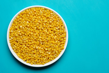 canned corn in white plate top view.  turquoise, light blue background