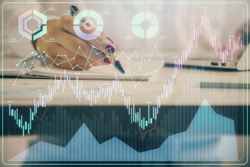 Double exposure of woman's hands making notes with forex graph hologram. Concept technical analysis.