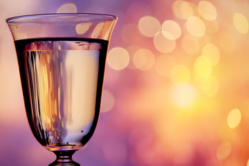 Glass with champagne sparkling wine on a festive background with lights and bokeh. The atmosphere of celebration and happiness.