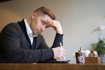 Pensive male with tablet in hands sitting at table