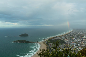 Fototapeta na wymiar ニュージーランド　タウンランガ湾の半島にあるマウント・マウンガヌイのマウアオの丘の麓から見えるビーチと街並みと虹