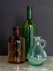 Green and Brown Glass Bottles with Jar on Marble table with Black Background Window Natural Light Still