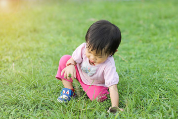Soft focus. Asian baby child girl practice to walking at the grass field. She falling and sitting at the ground. Development of baby aged of one year old. Kid Exercise for health.
