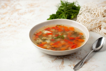 Hot fish soup with potatoes, red bell peppers, carrots and greens in a light plate on a light background. space for text