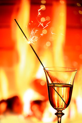Glass with sparkling champagne wine against the background of a burning fire in a fireplace. The cozy atmosphere of winter evenings by the fireplace, the celebration of winter holidays.