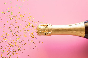 a bottle of champagne and a scattering of confetti. Christmas firecracker concept on pink background © itakdalee