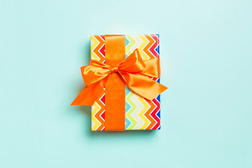 wrapped Christmas or other holiday handmade present in paper with orange ribbon on blue background. Present box, decoration of gift on colored table, top view with copy space