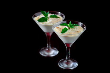 Two glasses of sweet milk dessert with coconut, peanuts and mint on black background with copy space