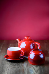 Red and white tea set with on dark wooden table with hot pink background.