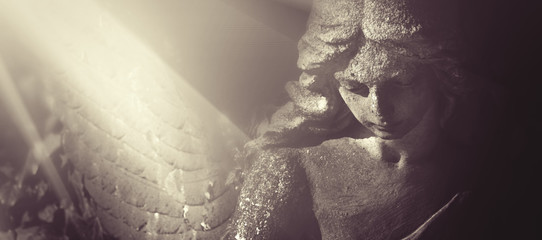 Sad wonderful angel in the rays of the sun. Antique statue.Horizontal image.