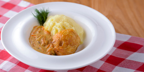Traditional cuisine, mashed potatoes with gravy, meat and dill served on a white plate on a plaid background