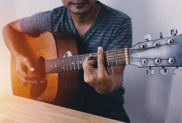 Obraz premium Man wearing a striped shirt playing guitar in his room with romantic atmosphere full of symphonic music.